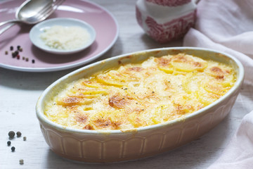 French dish Gratin Dauphinois in ceramic form on a light background. Rustic style.
