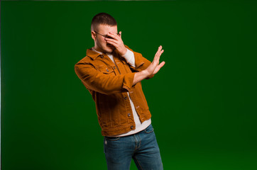 young handsome man covering face with hand and putting other hand up front to stop camera, refusing...