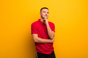 young handsome man looking happy and smiling with hand on chin, wondering or asking a question,...