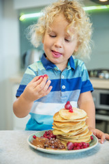 Little curly boy eating sweet pancakes
