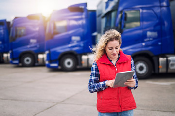 Truck driver holding tablet and checking route for new destination. In background parked truck vehicles. Transportation service. - obrazy, fototapety, plakaty