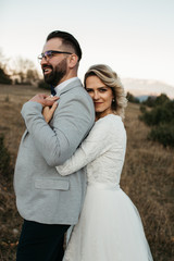 Beautiful couple having a romantic moment on their weeding day, in mountains at sunset. Bride is in a white wedding dress with a bouquet of sunflowers in hand, groom in a suit. Happy hugging couple.