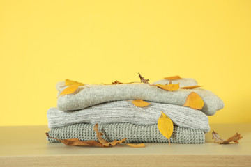 A stack of warm sweaters and autumn leaves on the table.