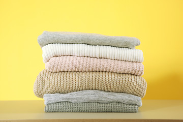 a stack of warm sweaters on the table on a colored background.