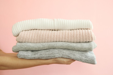 A stack of sweaters in female hands on a colored background. Warm clothes.