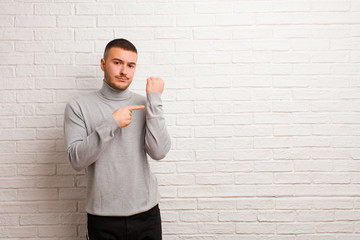 young handsome man looking impatient and angry, pointing at watch, asking for punctuality, wants to...