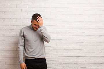 young handsome man laughing and slapping forehead like saying d‚Äôoh! I forgot or that was a...