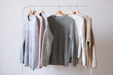Warm sweaters on a wardrobe hanger on a light background. Autumn, winter clothes.