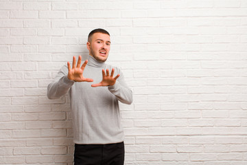 young handsome man feeling terrified, backing off and screaming in horror and panic, reacting to a...