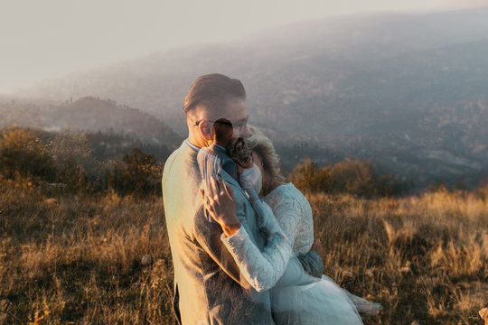 Beautiful couple having a romantic moment on their weeding day, in mountain, sunset.She is in a white wedding dress with a bouquet of sunflowers in hand,groom in a suit. Double exposure photo, hugged.