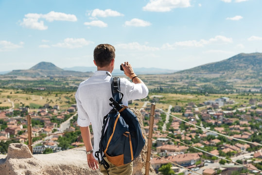 Man tourist with backpack taking pictures or footage with action camera on top of Uchisar castle.