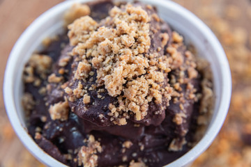 Acai in cup with peanut candy on wooden background with granola