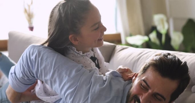 Kid daughter tickling dad lying on his back on sofa