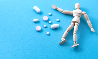 Heap of pills near miniature wooden human model at blue background. Harmful effects of medications concept