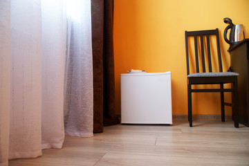 Small compact white refrigerator in the interior of a cramped studio apartment or hotel room