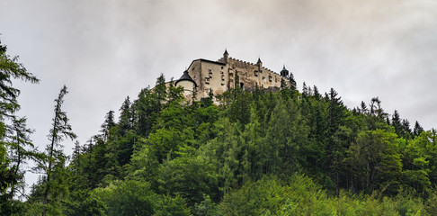 Hohenwerfen Castle is a medieval rock Alpine castle and history museum near Salzburg, Austrian Alps, Austria. It is surrounded by pine forests. Castle view on a rainy summer evening at sunset