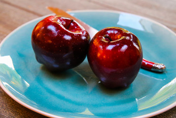 Close up of isolated two red dotted shiny isolated dessert apples on blue china dish with knife