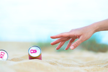 Hand reaching alcohol drink can on the beach.