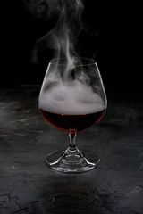 Glass glass with cognac filled with smoke on a dark background.