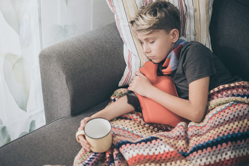 Sick boy sleeping with woolen blanket, hot water bottle and a mug. Sad teen with the flu rests...