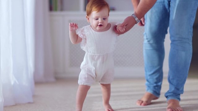 happy little baby girl learning to walk, toddling with father at home
