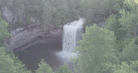 Ungraded, flat profile drone shot flying behind some trees and revealing a gushing Greeter Falls found in Altamont, Tennessee.