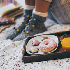 Young woman lying on colorful bed having breakfast on holidays. Morning in a cozy warm bedroom with natural juice Christmas cookies and and donut. Happy young girl thinking on wishes for the new year