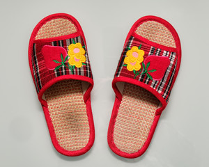 A pair of used red and colorful home slippers with flowers and strawberries on it lying on white...