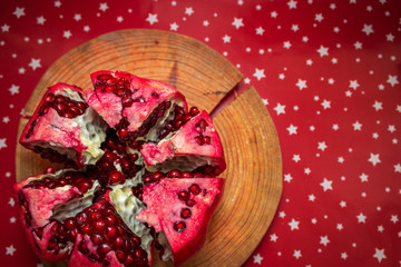 Pomegranate isolated on red paper background. Juicy red garnet on wooden stand. Slices of garnets. Flat lat with place for text. Copy space