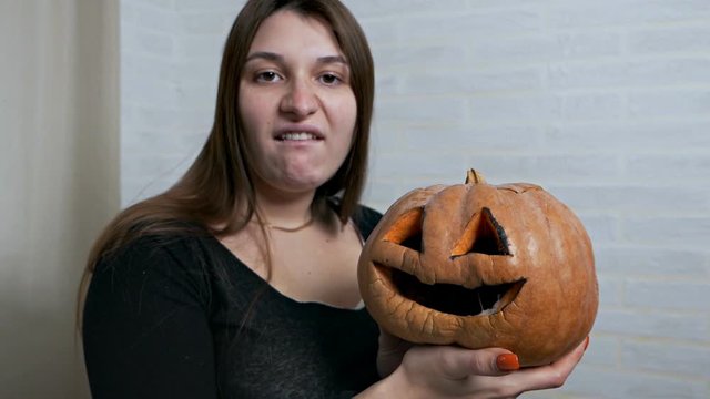 A young girl holds a missing pumpkin in her hands and wrinkles her face, makes various facial expressions. Pumpkin image