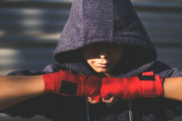 Young male hands with boxing bands ahead the face. Boy prepares for a boxe workout by wrapping his hand. Boxer ready to throw punches. Teenager Sport, youth, determination and training gym concept. - obrazy, fototapety, plakaty