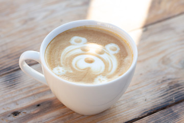 White сup of coffee on a wooden table. Cappuccino with a bear pattern and sunlight in mug.
