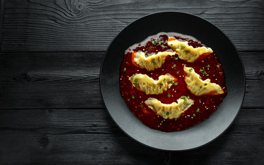 Steamed yaki Gyoza served on black plate with sweet chilli sauce and sesame seeds