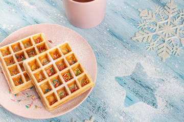 Belgian waffles with powdered sugar and confectionery sprinkles on the plate. Christmas and New Year mood are created by a star and snowflakes