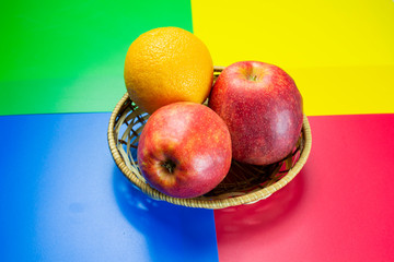 fresh apples in a straw basket with orange on a colored background