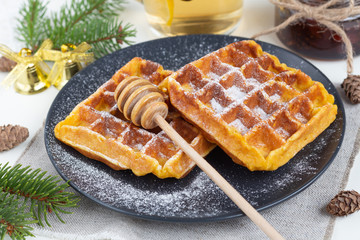 Belgian waffles sprinkled with icing sugar with a honey spoon on a black plate. Christmas mood is...