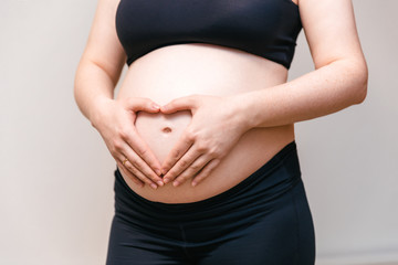 Image of the stomach of pregnant woman in the top and leggings, arms hugging her stomach. Pleasant expectation baby