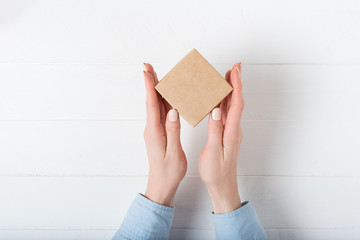 Small square cardboard box in female hands. Top view, white background - Powered by Adobe