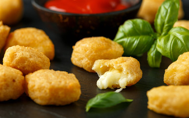 Fried mozzarella, cheddar cheese bites, balls with ketchup on rustic stone board