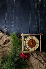 Golden vintage clock with pine branches and red berries on black wooden background. Merry Christmas, New Year eve and winter holidays concept. Minutes to midnight. Vertical shot, top view, copy space.