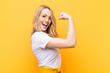 young pretty blonde woman feeling happy, satisfied and powerful, flexing fit and muscular biceps,...