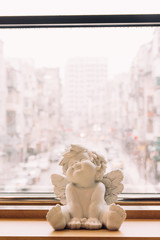 sculpture of an angel, decor, stands on the background of the city, an angel sits on a wooden table, windowsill. Valentine's Day. protection. Guardian