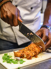 Chef at work cutting breaded chicken with big knife close up.