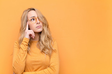 young pretty blonde woman with a concentrated look, wondering with a doubtful expression, looking...