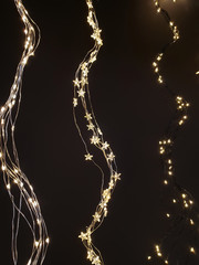 Star and sleeve Christmas lights, fairy lights hanging in a wave form next to each other on dark background.