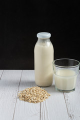 Healthy dairy free oat milk and oat flakes in glass bottle on white wooden background. Vegetarian and lactose free diet concept. Copy space for text.