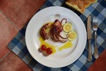 A plate of cooked small polyp and lemons garnished in olive oil on a ceramic table with old cutlery...