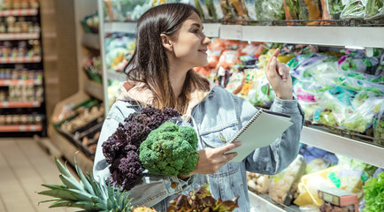 A young woman with a notebook buys groceries in the supermarket.