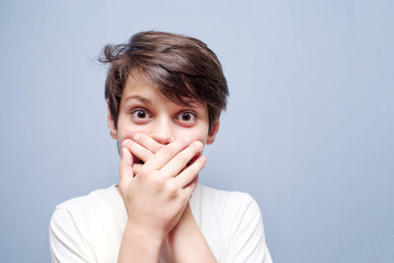 Boy covering his mouth with his hands against a blue background
