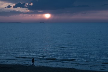 spacer brzegiem morza, zachód słońca nad Bałtykiem, pusta piaszczysta plaża pod koniec dnia, spokojne morze